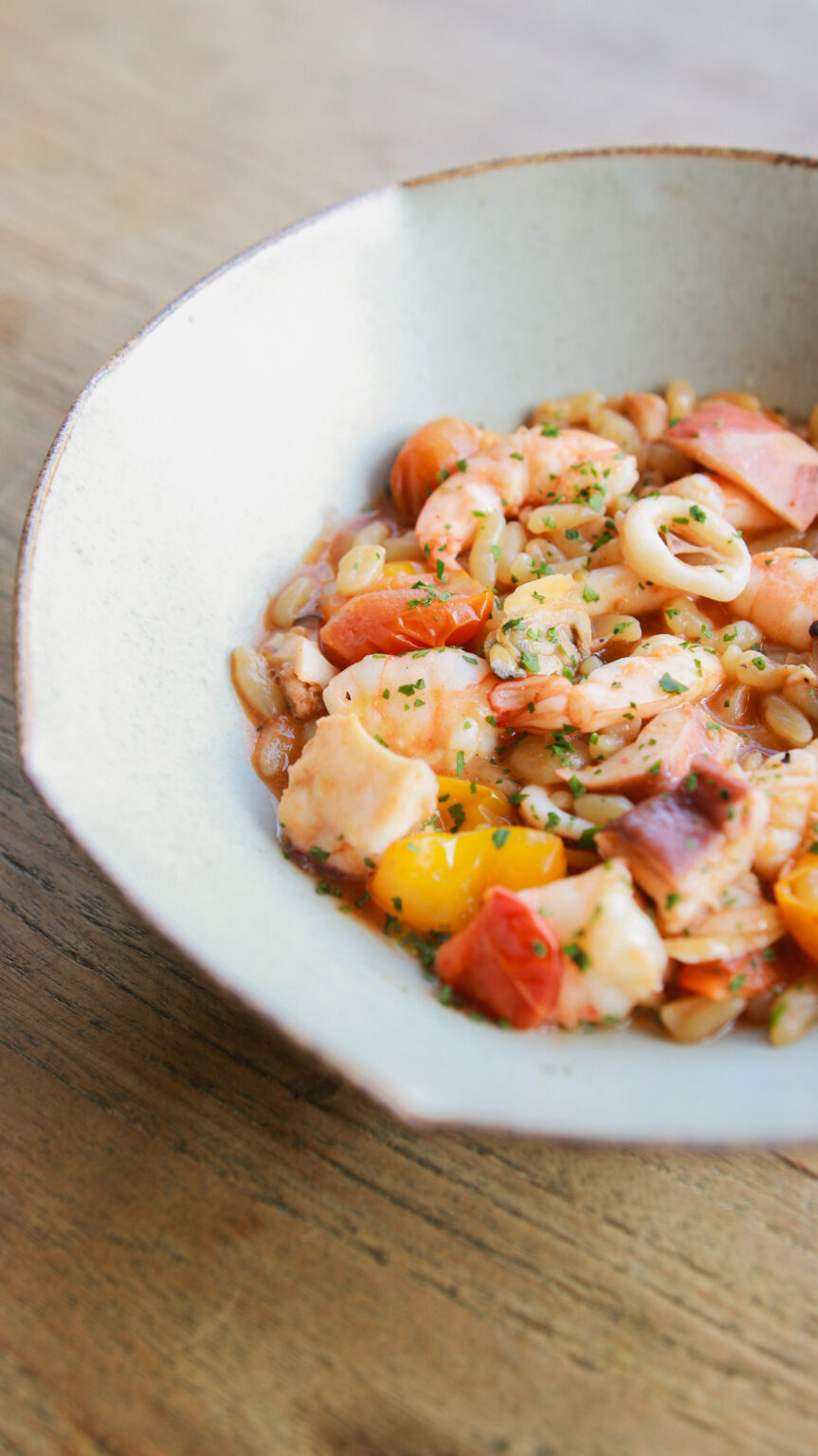 Seafood salad with prawns, calamari and tomato in a white bowl on the rooftop table