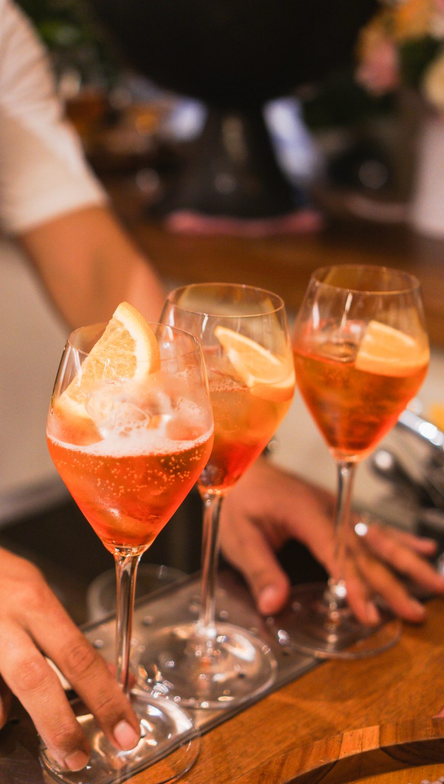 Hands holding bright orange spritz cocktails during early evening aperitivo hours